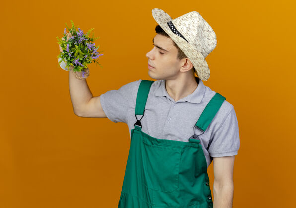 年轻自信的年轻男园丁戴着园艺帽捧着花盆看穿橙色男性