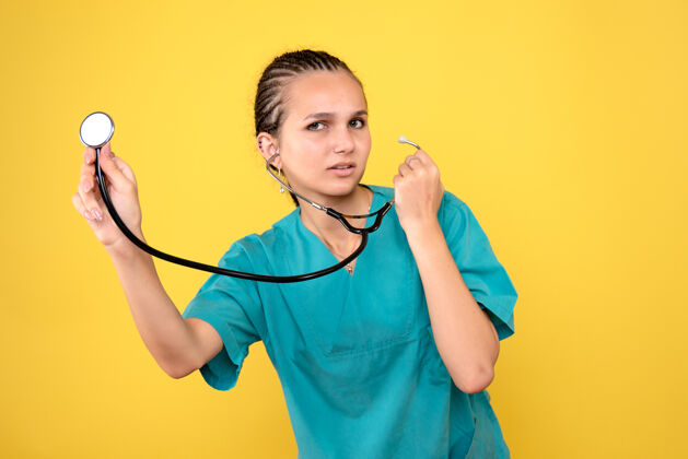 听诊器黄色墙壁上穿着带听诊器的医用衬衫的女医生的正视图情绪人仪器
