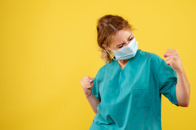 成人身着医疗服 戴着无菌口罩的年轻女医生在黄墙上欢呼雀跃的正面图套装肖像支持