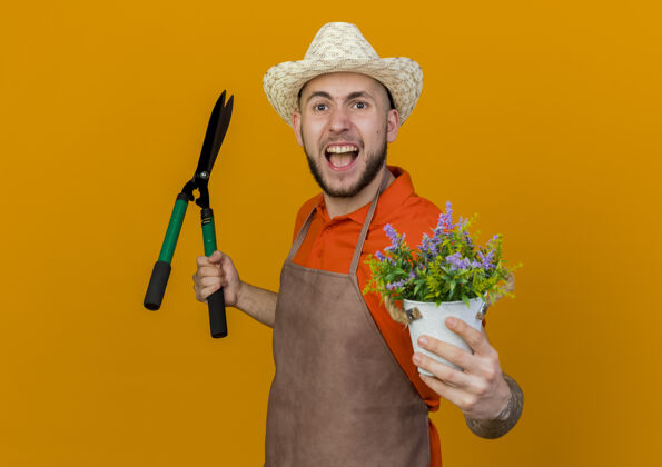 磨损恼怒的男园丁戴着园艺帽 手里拿着剪子和花盆里的花橘子帽子烦恼