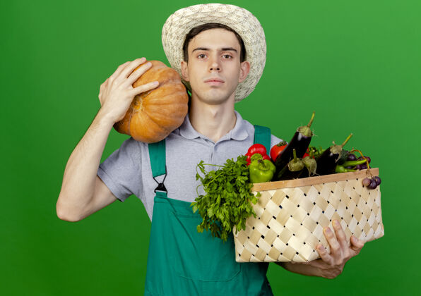 复制自信的年轻男园丁戴着园艺帽 手里拿着菜篮和南瓜看信心南瓜篮子