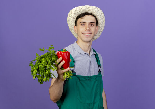微笑微笑的年轻男园丁戴着园艺帽 手里拿着红辣椒和香菜男性空间红色