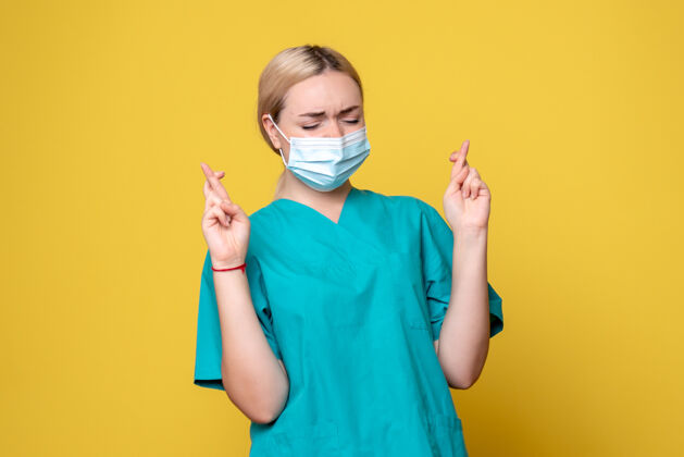 绝育身穿医用衬衫 戴着消毒口罩的年轻女医生的正视图交叉在黄色的墙上人脸十字架
