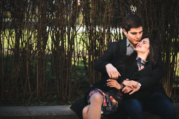 站在一起美丽的女孩和她的男朋友一起在公园的长凳上休息现代两个调情