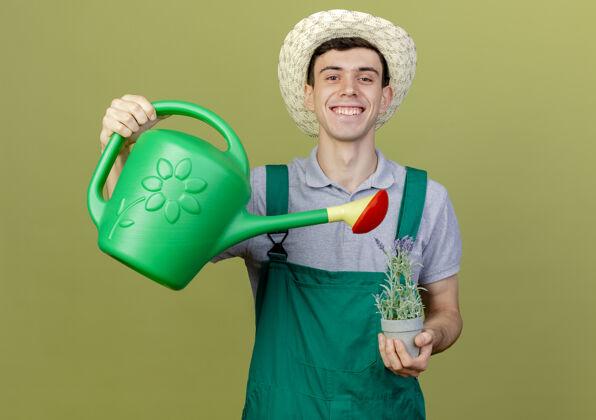 浇水微笑的年轻男园丁戴着园艺帽 假装用水罐在花盆里浇花花复制园艺