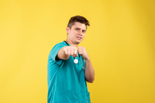 显示身穿医疗服的男医生的正面图 他的拳头在黄色的墙上前面健康医疗