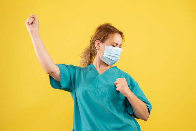 医疗黄色墙壁上穿着医疗服 戴着口罩的女医生的正视图人正面流行