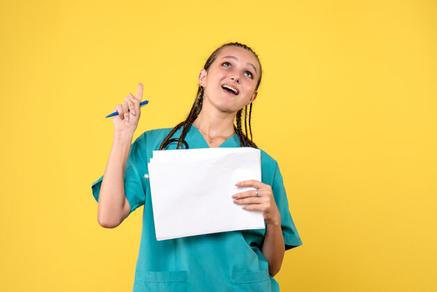 套装黄墙上穿着医疗服拿着纸的女医生的正视图快乐纸正面