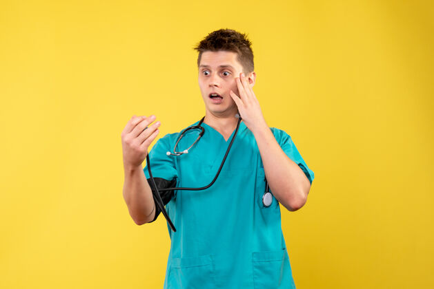 人身穿医疗服的男医生在黄色墙壁上检查压力的前视图成人医疗医院