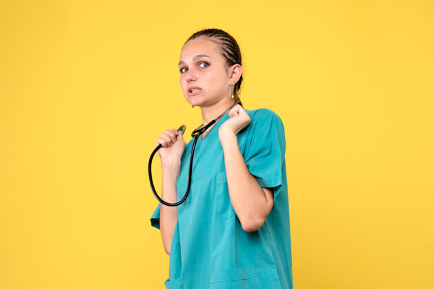 医生黄色墙壁上穿着带听诊器的医疗服的女医生的正视图仪器人女医生