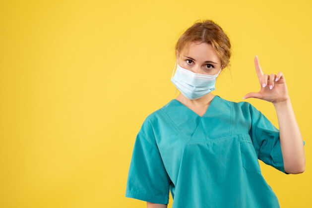 健康黄墙上年轻女医生穿着医疗服 戴着口罩的正面图支持医生年轻女医生