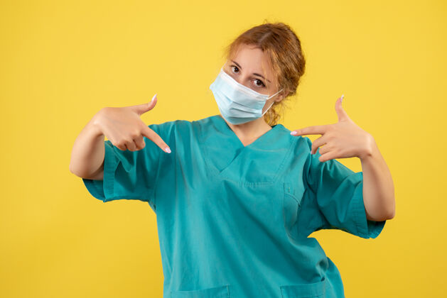 快乐黄墙上年轻女医生穿着医疗服 戴着口罩的正面图面具肖像年轻女医生