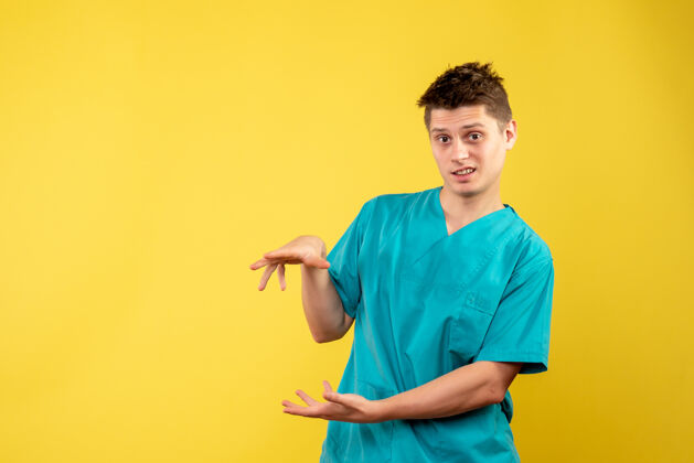 健康黄色墙壁上穿着医疗服的男医生的正视图套装医院男性医生