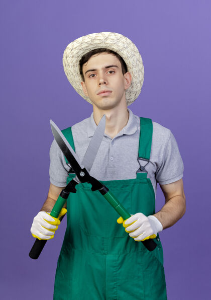 剪子自信的年轻男园丁戴着园艺帽和手套拿着剪刀年轻手套紫色
