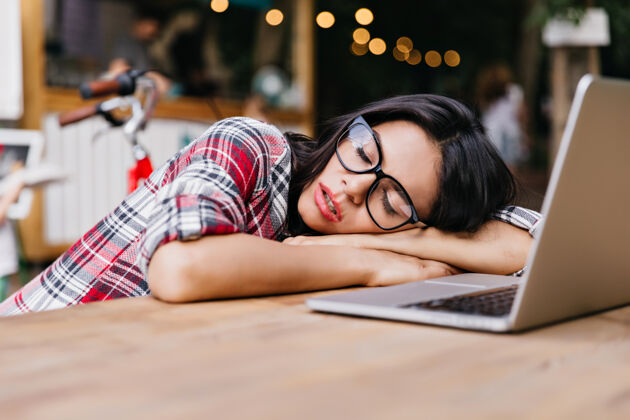 可爱黑头发的漂亮学生睡在电脑旁迷人的女自由职业者的户外肖像 穿着格子衬衫 下班后休息青年人累