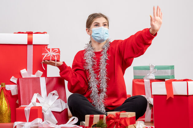 礼物正面图：年轻女性戴着无菌面具围坐在圣诞礼物旁生活围着病毒