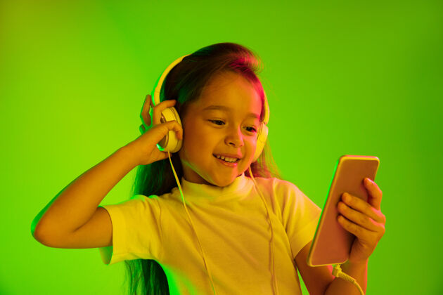童年美丽的女性半身像 隔离在霓虹灯下的绿色背景上年轻感性的女孩人类情感 面部表情概念使用智能手机进行虚拟博客 自拍 聊天 游戏孩子迪斯科巴塞罗那
