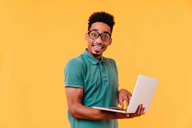 表情灵感来自戴着眼镜的非洲学生手持白色笔记本电脑无忧无虑的黑人男性自由职业者微笑着自信微笑室内