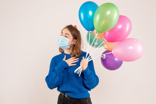 情感正面图：戴着消毒面具的年轻女性手持五颜六色的气球气球公园吹