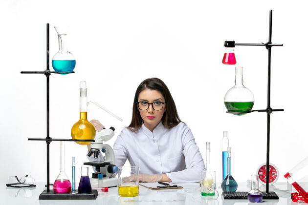 实验室前视图穿着白色医疗服的女化学家坐在浅白背景上实验室病毒冠状病毒大流行科学套装前面病毒