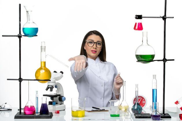 科学前视图穿着白色医疗服的女化学家坐在白色背景的科学大流行病毒冠状病毒实验室里 拿着溶液大流行视图套装