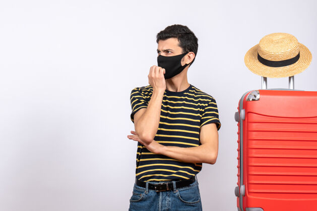 视图正面图：戴着黑色面具的年轻游客站在红色手提箱旁 看到了什么黑色工作室脸