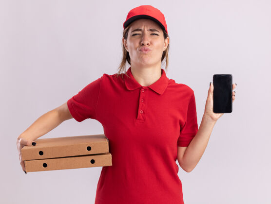 年轻穿着制服的年轻漂亮的送货女孩拿着披萨盒和白色的电话盒子成人姿势
