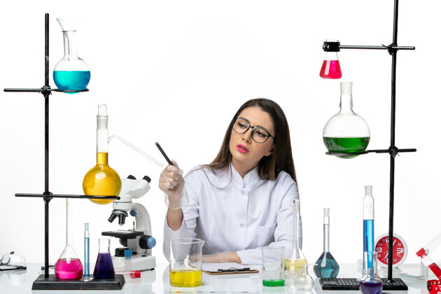 瓶子前视图穿着白色医疗服的女化学家正坐在一个白色背景的科学病毒冠状病毒大流行实验室里 拿着溶液写笔记套装杯子医学