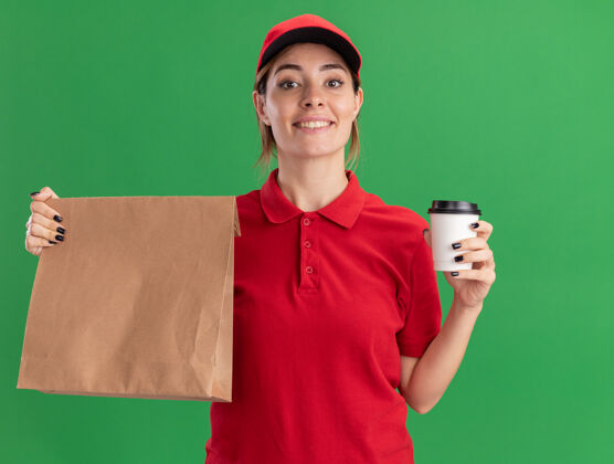 漂亮微笑着的年轻漂亮的女送货员 穿着制服 手里拿着纸包和纸杯 站在草地上年轻送货包装