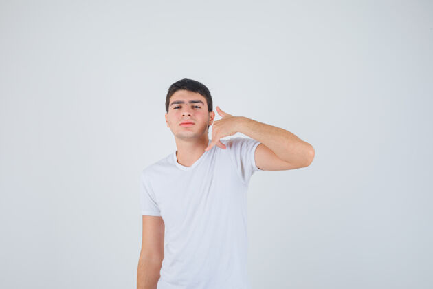 思想身穿t恤的年轻男性 展现电话手势 看起来自信 正面照年轻站立正面