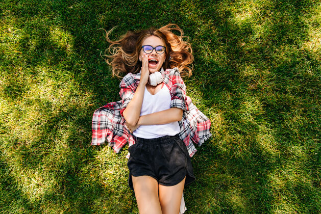 草地迷人的苗条女孩躺在草坪上优雅的金发年轻女子在草地上冷的头顶镜头微笑音乐快乐