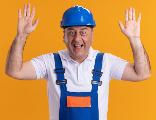 手兴奋的白人成年建设者身着制服站在橙色上举手建筑工人站起来举起