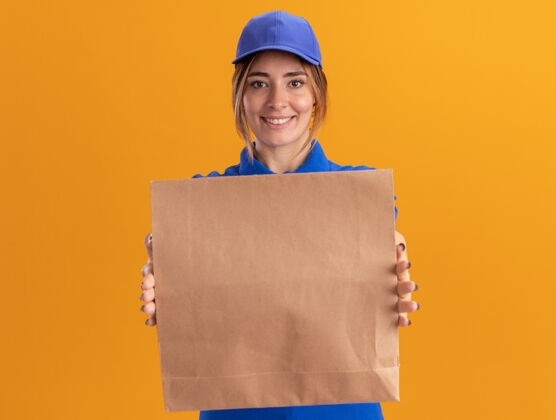 姿势微笑着的年轻漂亮的送货女孩 穿着制服 手里拿着橙色的纸食品包制服包装漂亮