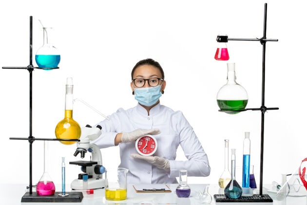 实验室前视图穿着医疗服的女化学家 戴着面具 白色背景上拿着红色的时钟病毒实验室化学冠状病毒-飞溅视图科学医生