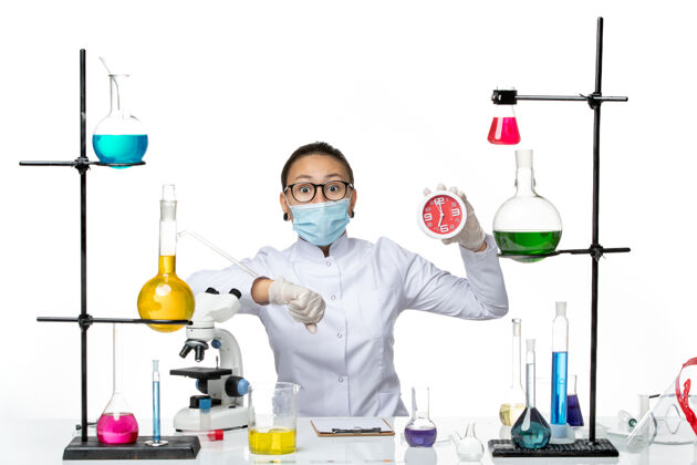 实验室前视图穿着医疗服的女化学家戴着面具拿着时钟看着她手腕上的白色背景病毒实验室化学冠状病毒-飞溅病毒化学医学