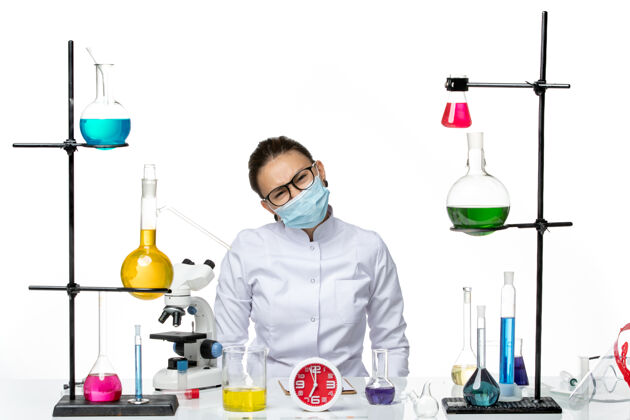 医学前视图穿着医疗服的女化学家戴着面罩坐在白色地板上 解决方案病毒实验室化学科维德飞溅坐着医生面罩