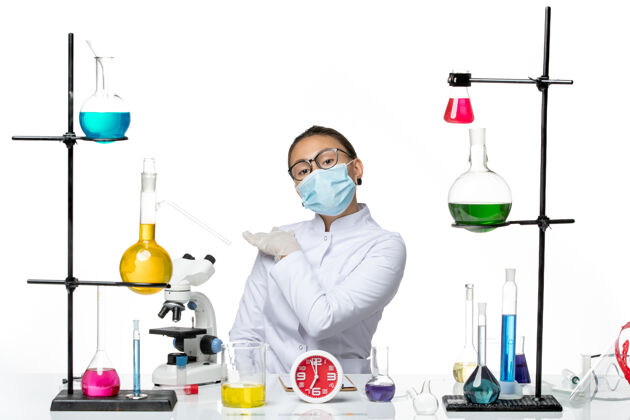 实验室前视图穿着医疗服的女化学家带着面罩坐在白色背景上的溶液飞溅病毒化学冠状病毒-实验室医生套装化学