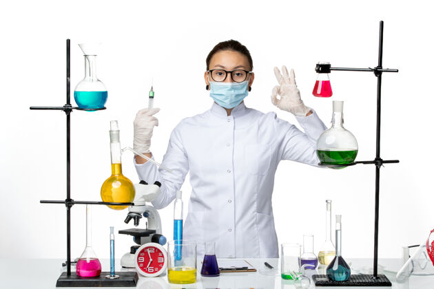 专业正面图白色办公桌上穿着医疗服的女化学家戴着口罩拿着针剂病毒化学实验室covidsplash注射外套实验室
