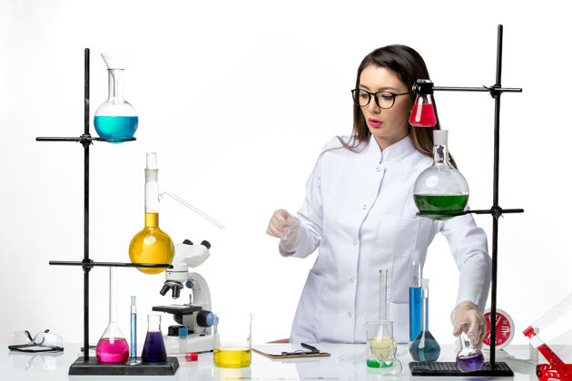 套装正面图：穿着无菌医疗服的女化学家站在桌子旁 拿着浅白背景病毒疾病的解决方案-大流行科学医学科学桌子