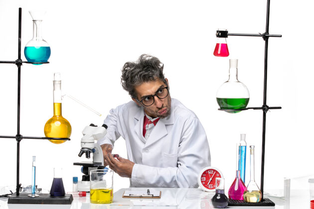 实验室前视图身着医疗服的男科学家坐在桌子前 浅白背景上有解决方案-实验室病毒健康化学桌子前面实验室外套
