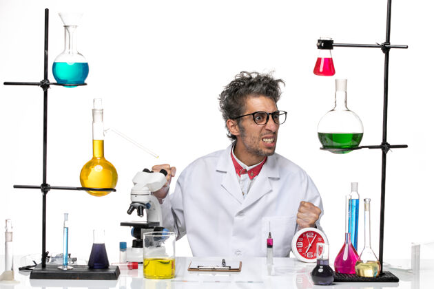 医疗前视图穿着医疗服的男科学家坐在桌子前 用白色背景的解决方案研究实验室病毒健康化学人职业医生