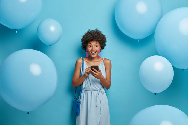社交这张照片是一位快乐的女士在公司聚会上的照片 她穿着蓝色的衣服 拿着智能手机 惊讶地从正式的丈夫那里得到意想不到的信息 在装饰物旁边摆着气球服装单色年轻人