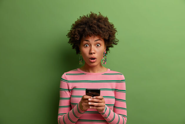 短信可爱的惊诧女人使用在线应用程序 使用手机在社交网络中聊天 惊诧地阅读惊诧的新闻 惊诧地收到消息 站在室内科技概念打字无线年轻
