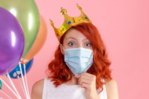 护士正面图：年轻女性手持彩色气球 戴着无菌面具站在粉红色的椅子上正面脸肖像