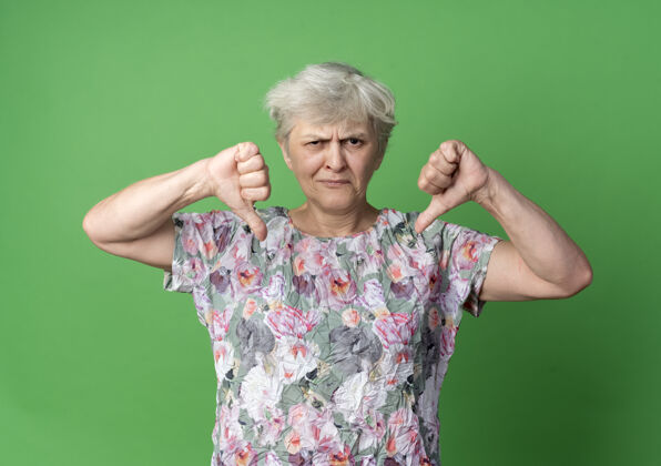 老的不高兴的老妇人竖起大拇指 两只手被隔离在绿墙上老的手绿的