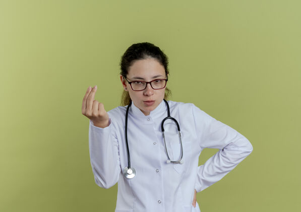 听诊器年轻的女医生 穿着医用长袍 戴着听诊器 戴着眼镜 做着指尖的姿势 手放在臀部医疗眼镜女人