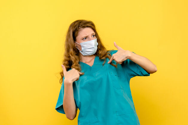 肖像黄色墙上戴着无菌口罩的女医生的正视图绝育医学制服