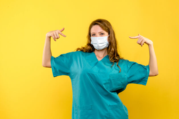 药黄墙上戴着面具的女医生的正视图流行病肖像黄色