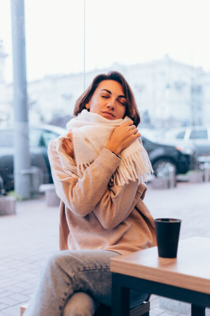 窗户一个女孩在舒适的咖啡馆里用一杯热咖啡取暖羊毛肖像女人