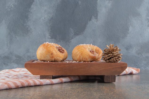甜点松果旁边有两块美味的饼干放在大理石木板上美味可口糕点